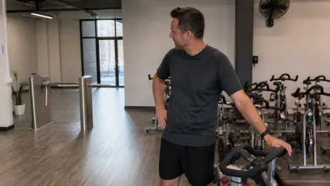 A gym manager looking toward a plain entrance gate beside stationary bikes in a natural fitness studio