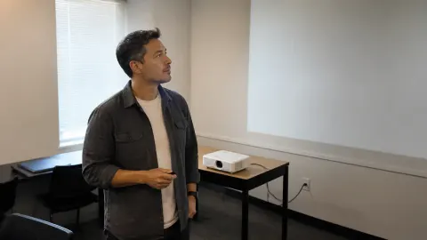 A small-business owner evaluating a blank projected demonstration in a plain meeting room
