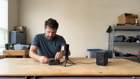 A small-business technical builder checking a microphone, speaker, cable, and plain voice gateway on a workbench